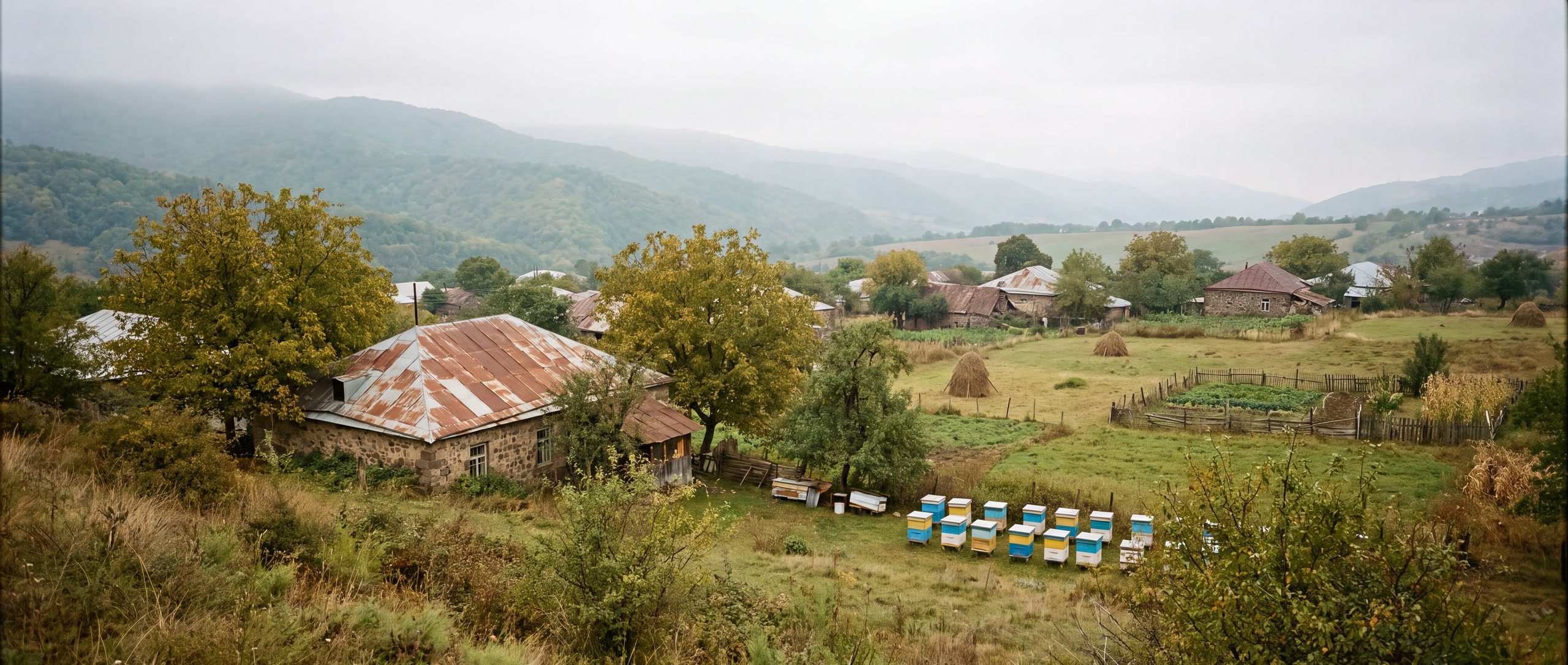 Een dorp in Tavush met golfplaatdaken, hooibergen en bijenkasten aan de veldrand