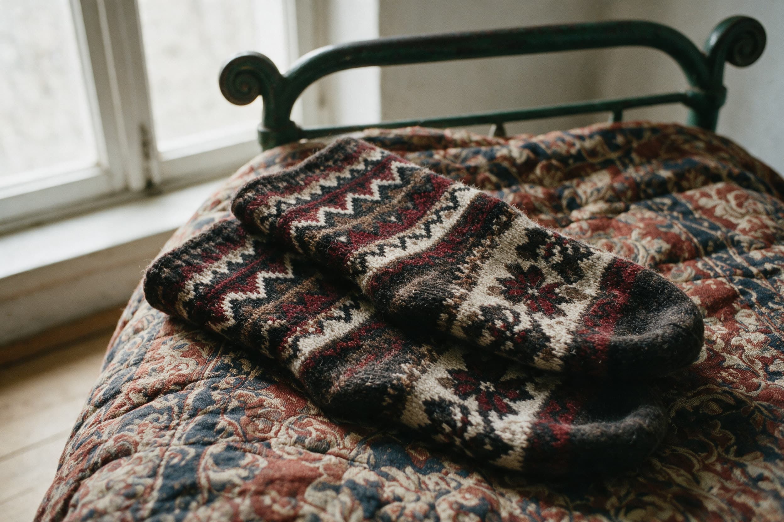 Des chaussettes de laine tricotées main sur un édredon à motifs, sur un lit en fer