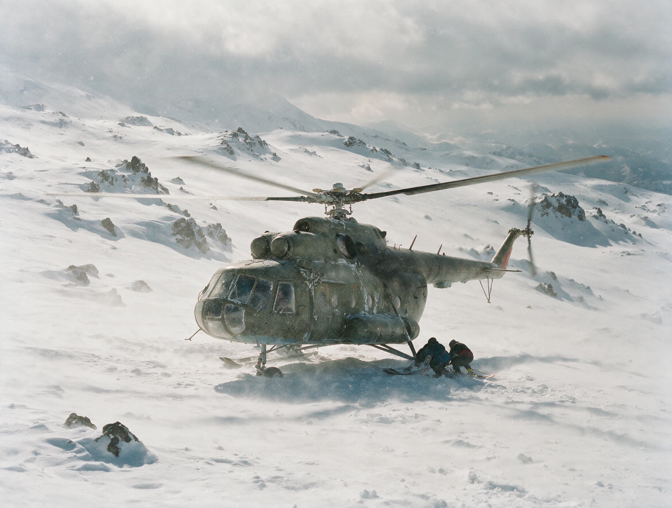 Mi-8 auf einer Schneeschulter des Aragaz, zwei Skifahrer geduckt an der Kufe