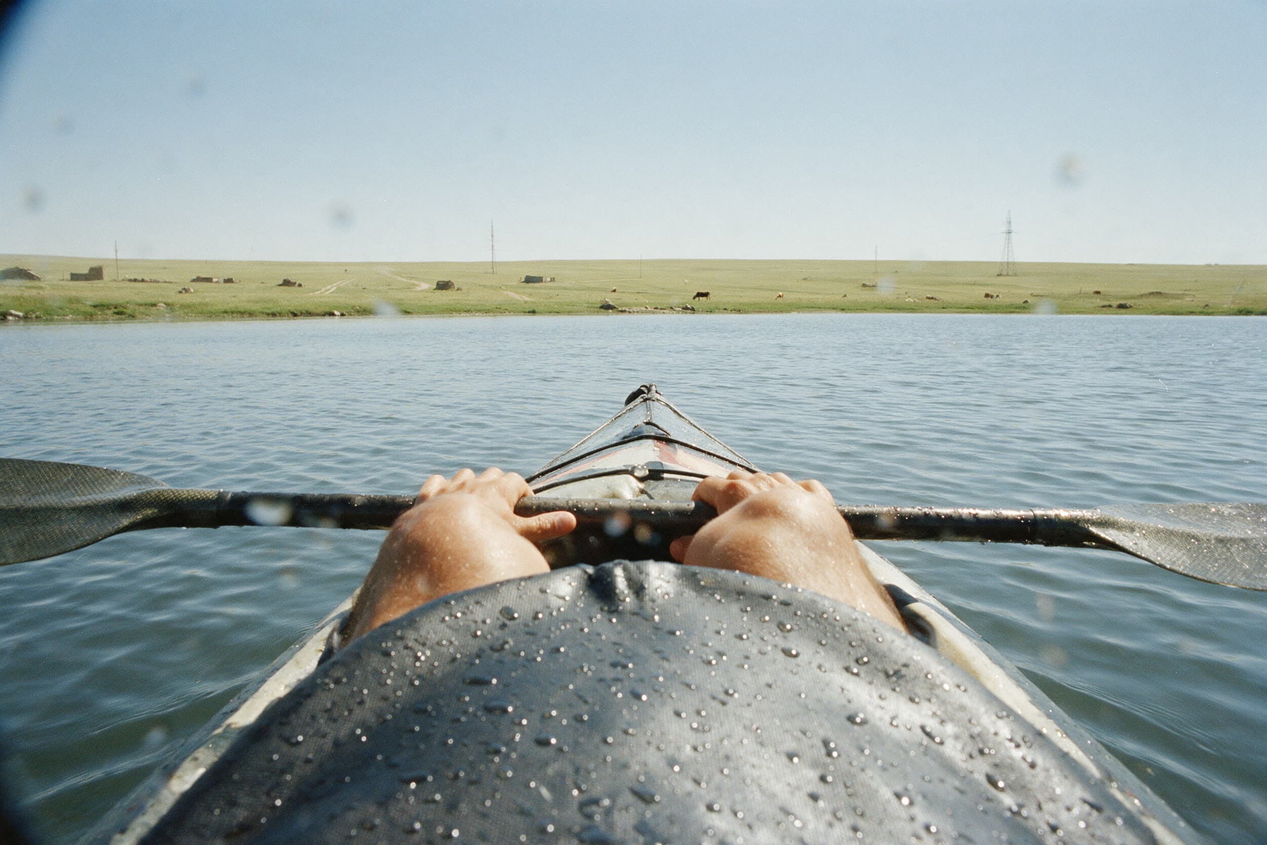 Vue depuis le cockpit d'un kayak, par-dessus la jupe et une pagaie mouillée, sur l'eau libre