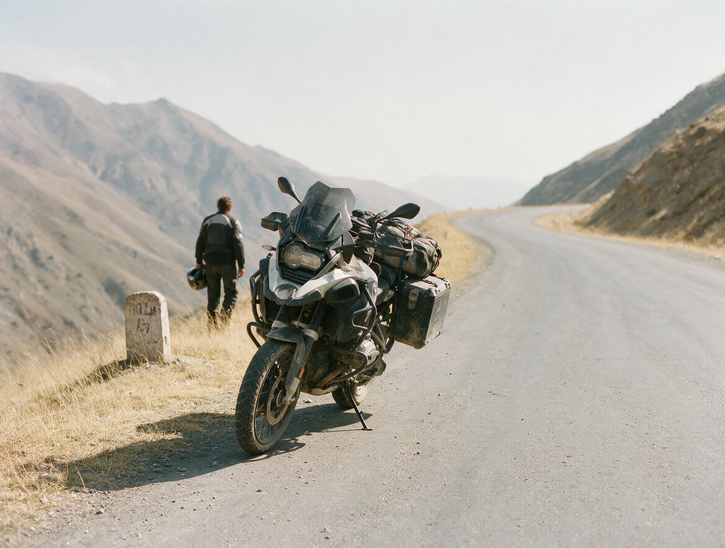 Bepacktes Reisemotorrad am leeren Passweg, der Fahrer mit dem Rücken zur Kamera
