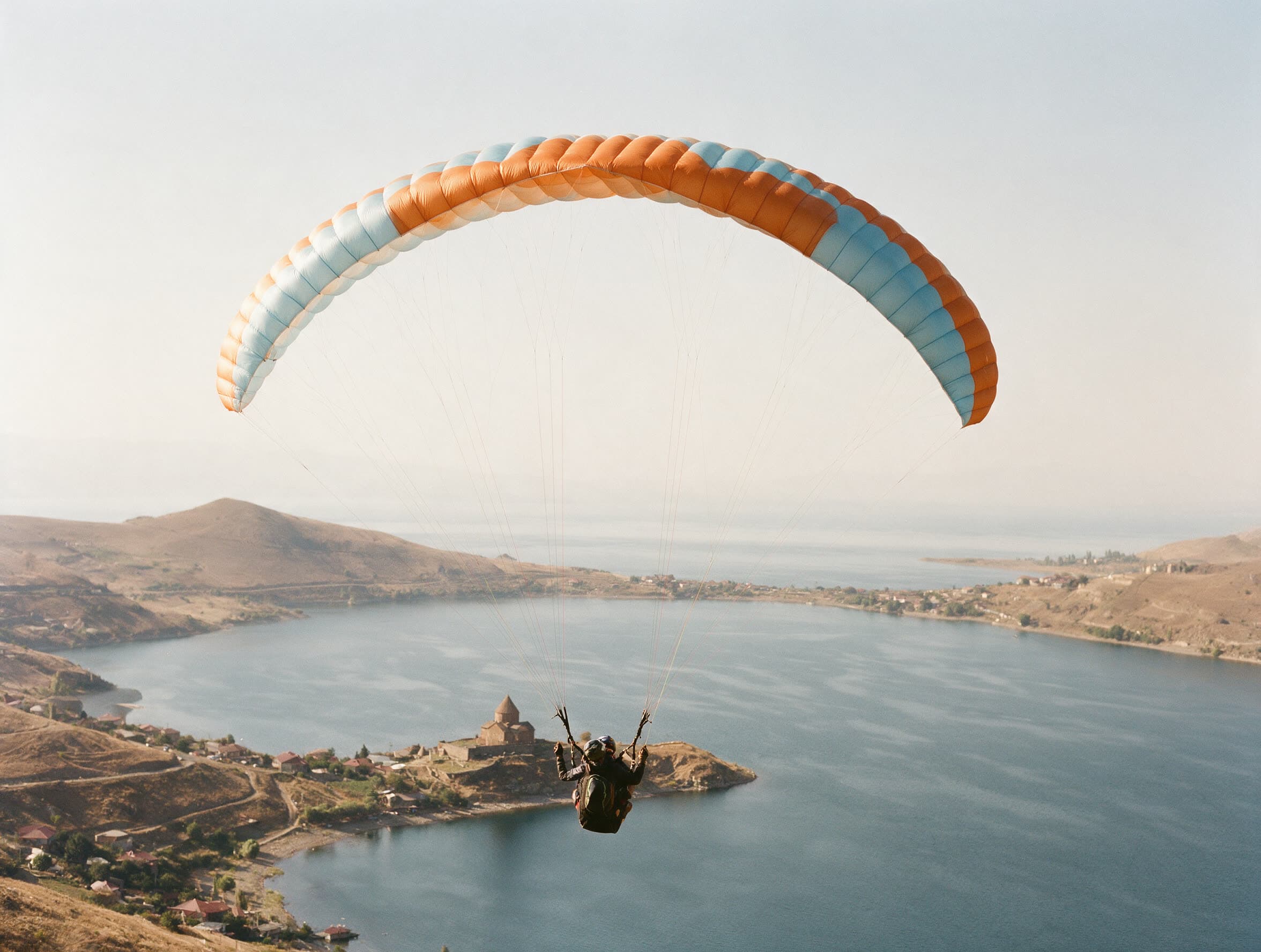Tandem-Gleitschirm von unten gegen blassen Himmel über dem Sewansee