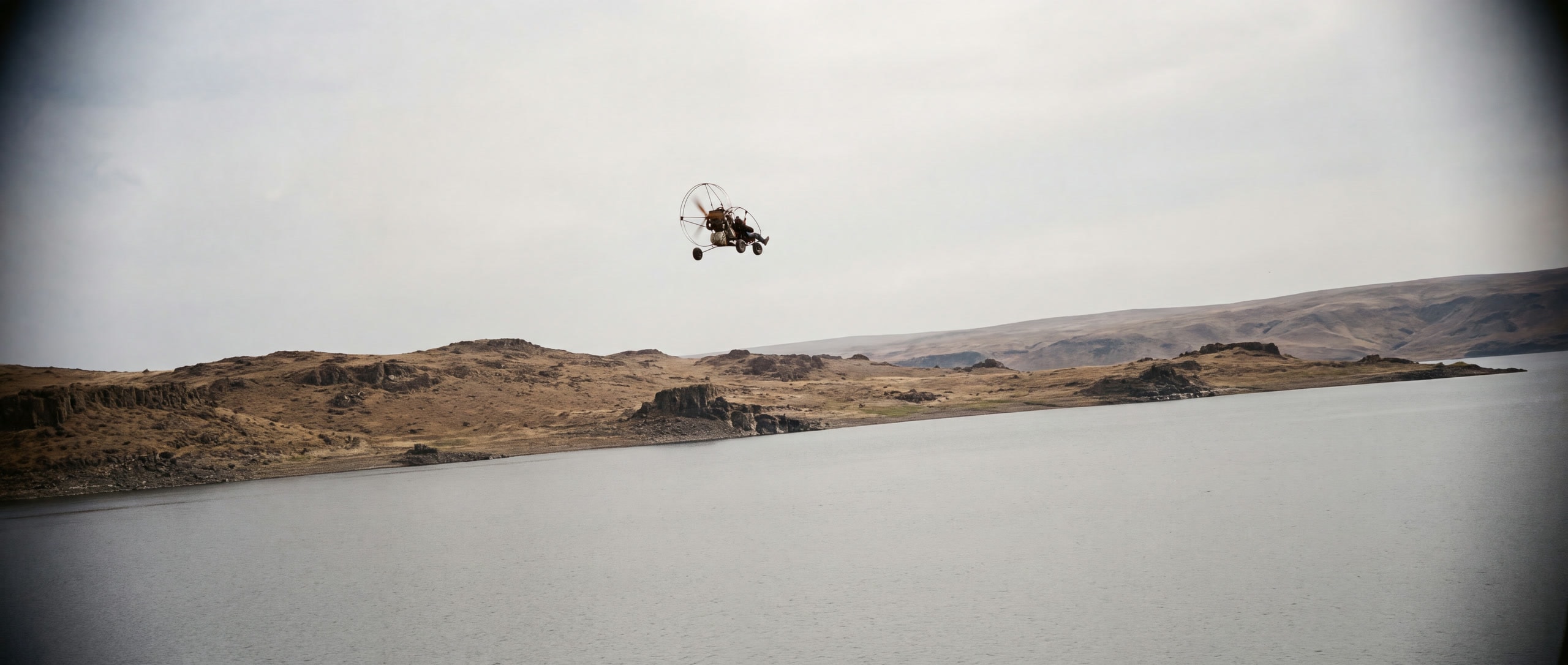 Un paramoteur pendulaire petit dans le ciel au-dessus du barrage d'Azat et de collines nues