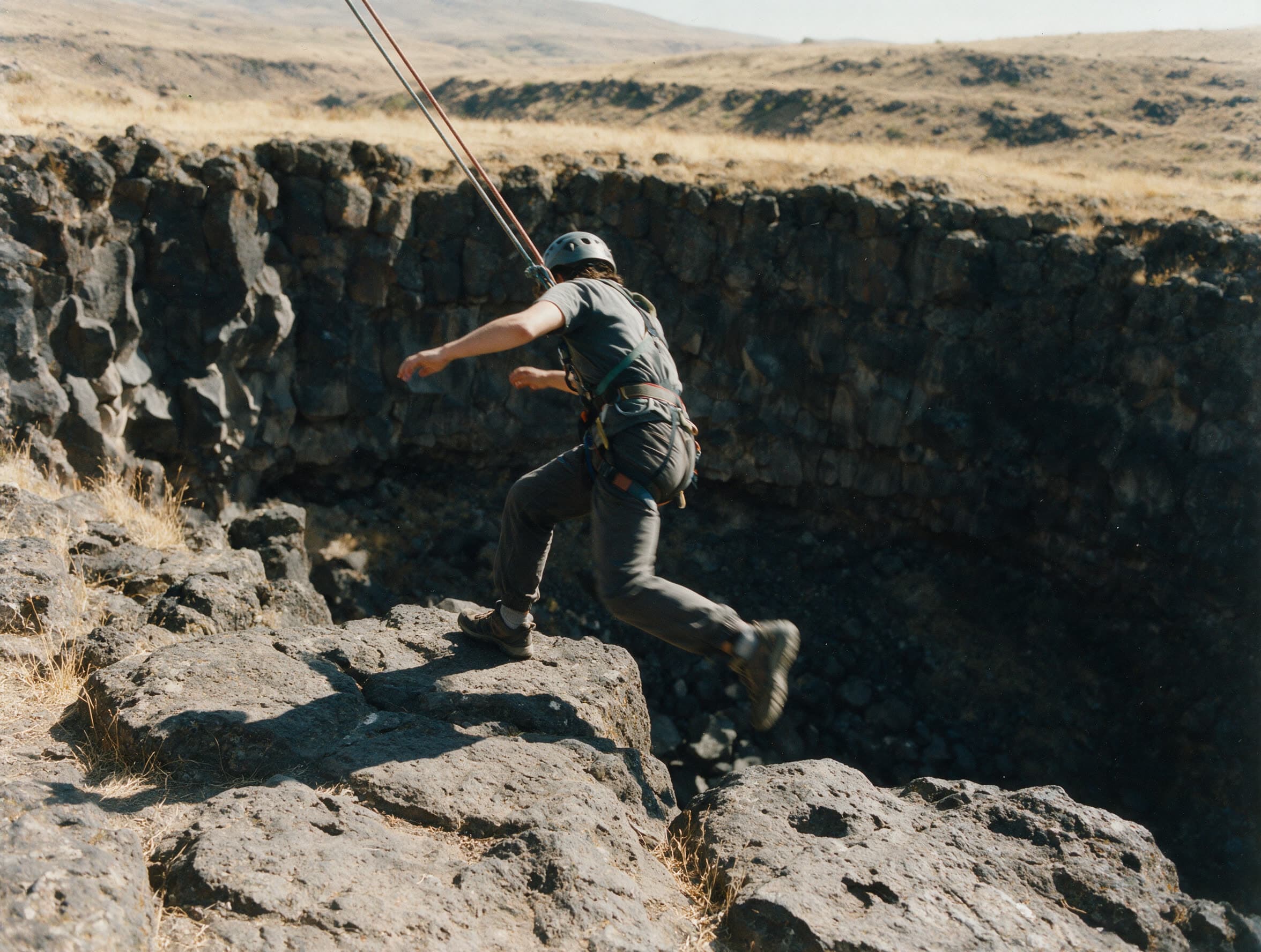Person im Klettergurt im Moment des Absprungs von einer Basaltkante in der Ararat-Region
