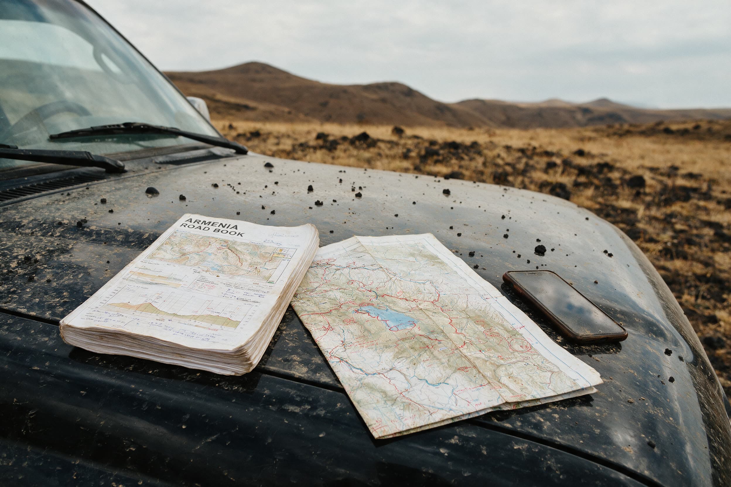 Een roadbook op de stoffige motorkap van een terreinwagen, droog gras en lavagrind eromheen