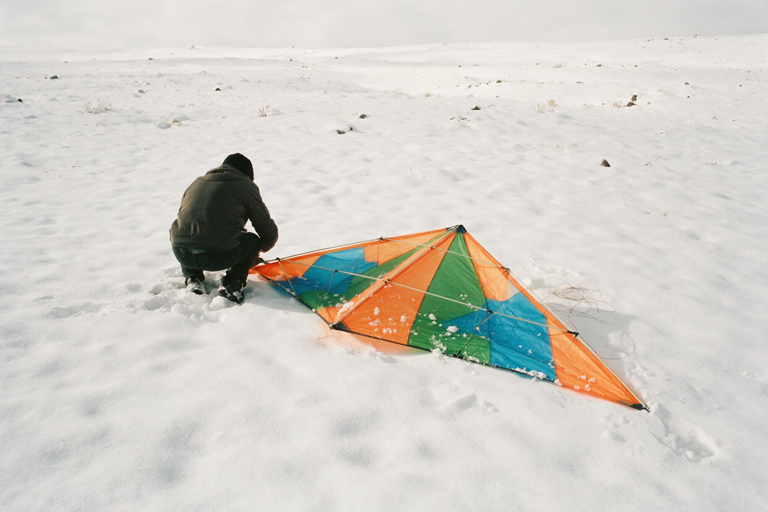 Kite wird auf dem Schnee zusammengelegt, eine Person kniet mit dem Rücken zur Kamera