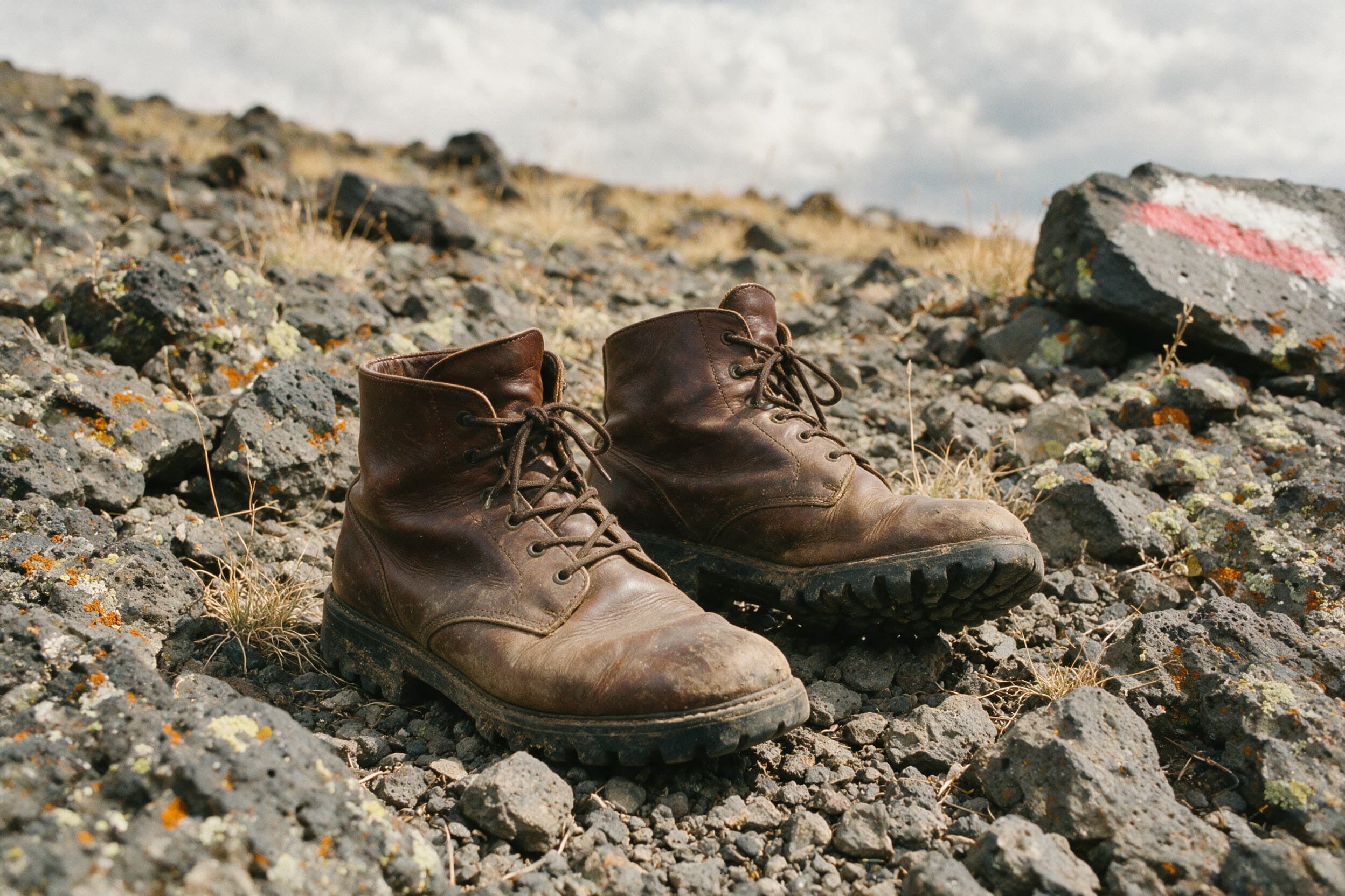 Abgetragene Wanderstiefel auf grauem Vulkanschotter, Wegmarke auf dem Fels
