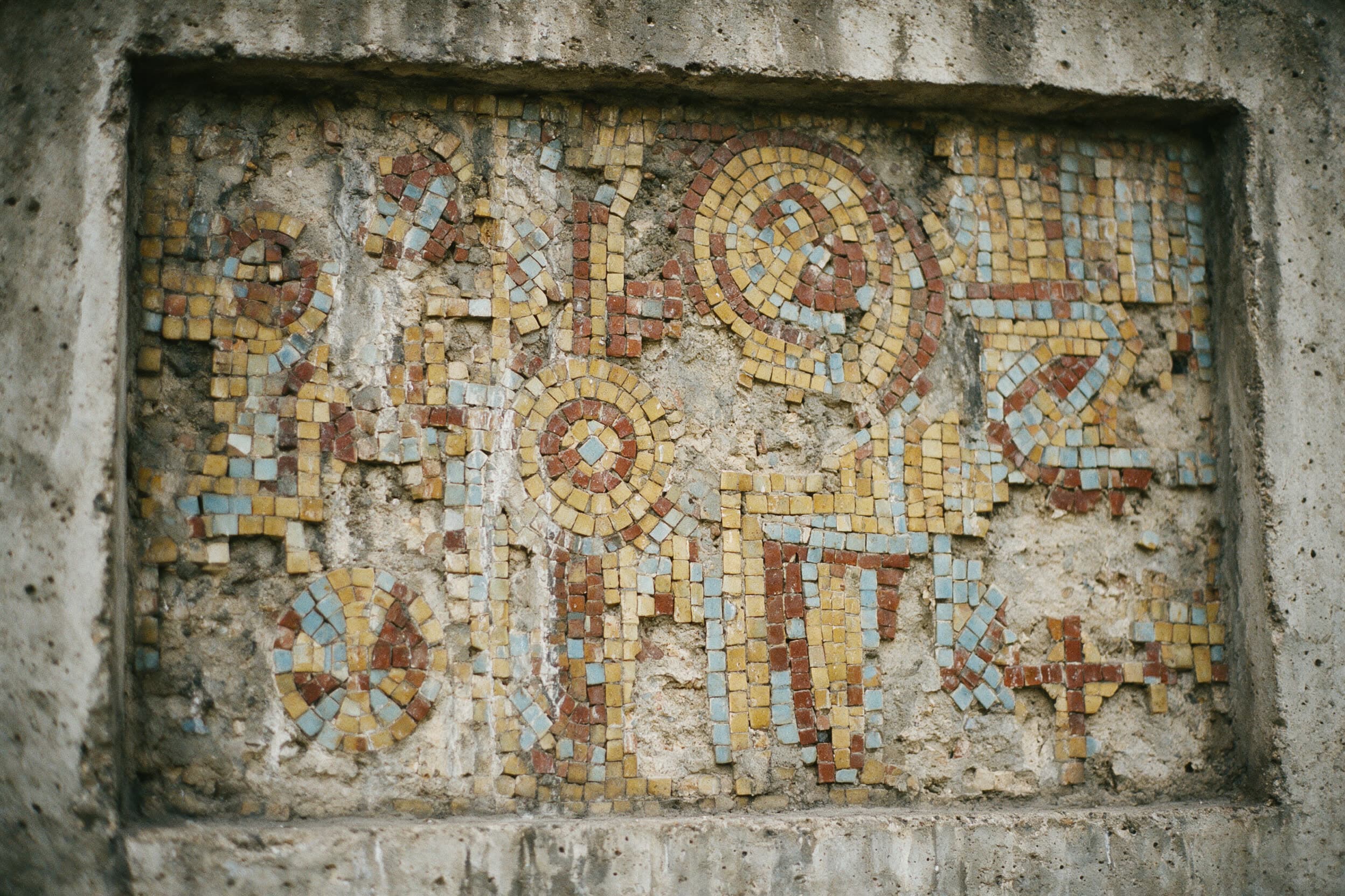 Verblasstes sowjetisches Mosaik an einer Betonwand, viele Steine fehlen