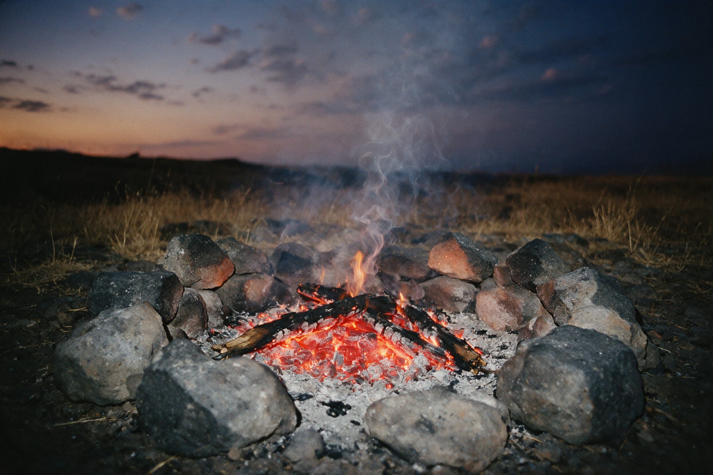 Heruntergebranntes Lagerfeuer in einem Ring aus Basaltsteinen in der Dämmerung