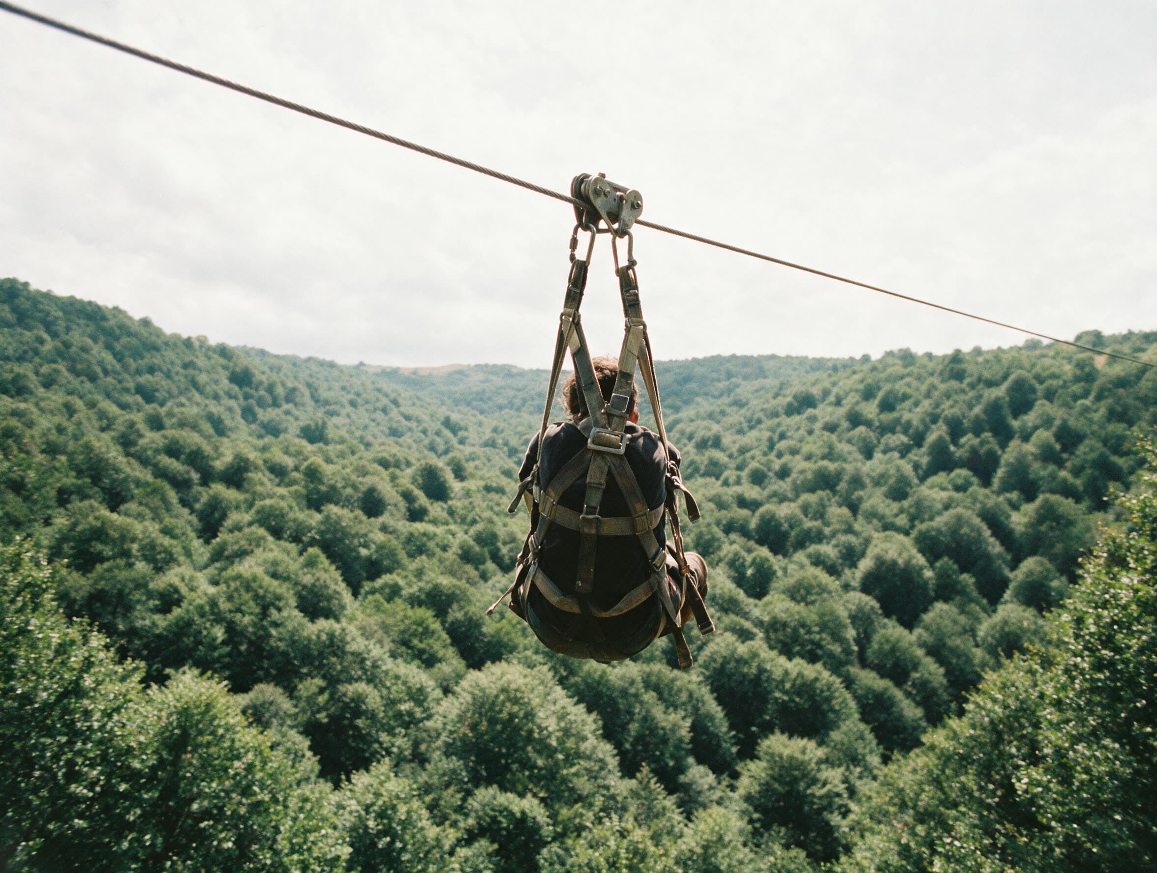 Person an der Zipline über einem Laubwaldtal in Tawusch