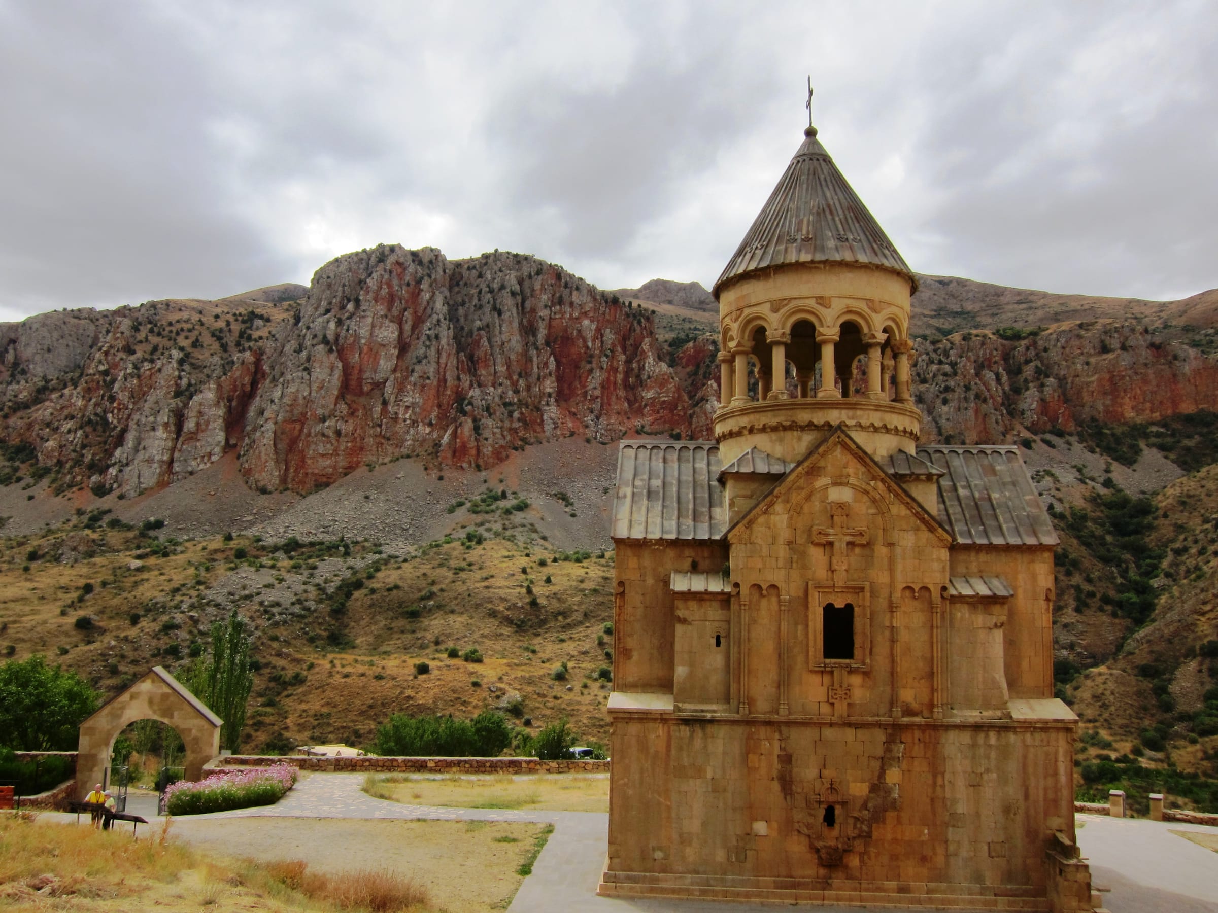 Surb Astvatsatsin church at Noravank standing before layered red cliffs under a clouded sky